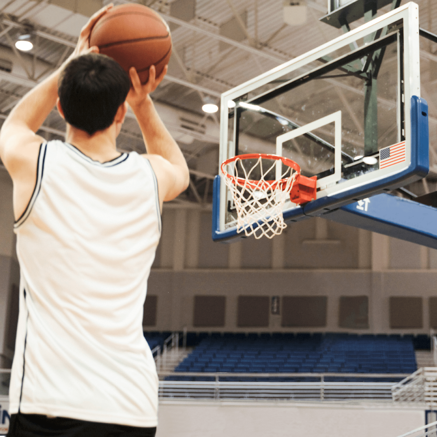 An athlete in a gym in front of a basketball hoop about to shoot a basketball at the hoop.